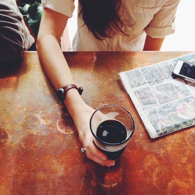 A woman holds on to her pint glass of stout beer. The local newspaper sits on the copper bartop.